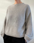 Photo of a woman wearing a beige version of the Bondi Sweater - a hand knit sweater by Berthyknit worked in double moss stitch. 
